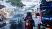 MAKASSAR. Un equipo de Policía de Indonesia rocía con desinfectante un coche circulando por una calle. 