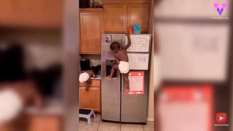Un niño de dos años escala una nevera para coger una piruleta Un niño de dos años escala una nevera para coger una piruleta