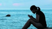 CONECTADA. Una mujer consulta su teléfono móvil en una playa durante el verano.