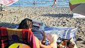 Una mujer ojea la portada de Diario JAÉN en la playa, ante la curiosidad de su bebé. / Diario JAÉN. 