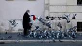 EN ITALIA. Una mujer con mascarilla da de comer a las palomas en una céntrica plaza de la ciudad de Roma.