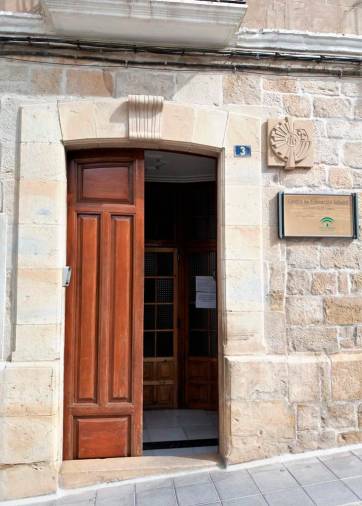 <i>Puerta de entrada, flanqueada por el escudo de Hermanas Mercedarias del Santísimo Sacramento y el cartel anunciador de Centro de Educación Infantil - Junta de Andalucía. </i>