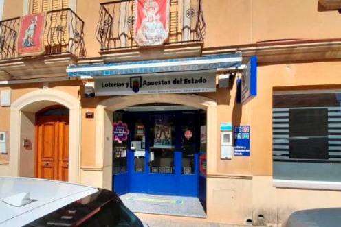 <i>Puerta de la administración ubicada en la calle Real, en Navas de San Juan, donde se ha vendido el número 33.478. / Loterías y Apuestas del Estado. </i>