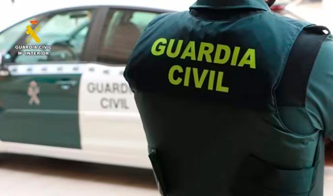 <i>Un agente de la Guardia Civil junto a un vehículo oficial. / Guardia Civil.</i>