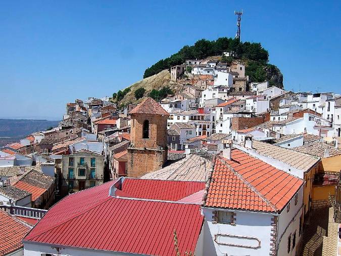 <i>Vista del caserío abigarrado al monte de la atalaya y al peñasco. En el centro emerge el campanario de la iglesia parroquial de San Pedro Apóstol. </i>