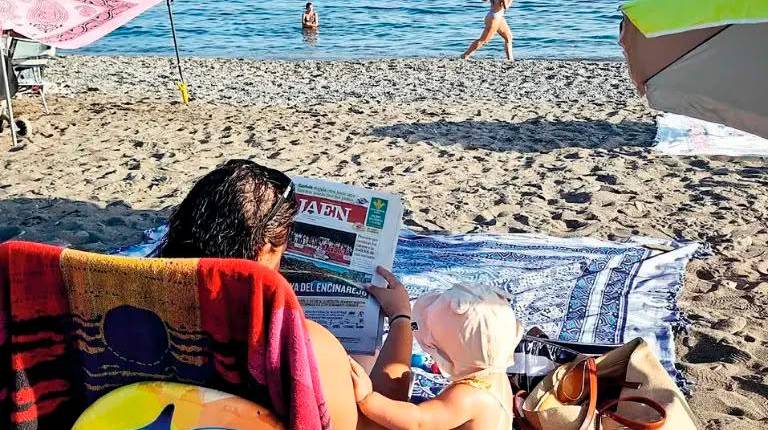 <i>Una mujer ojea la portada de Diario JAÉN en la playa, ante la curiosidad de su bebé. / Diario JAÉN.</i>