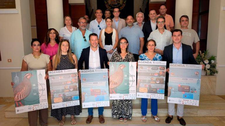 <i>Autoridades locales y organizadores, posa para una fotografía promocional en la escalera interior de un edificio institucional para presentar la III Feria de la Perdiz de La Carolina. / Junta de Andalucía. </i>