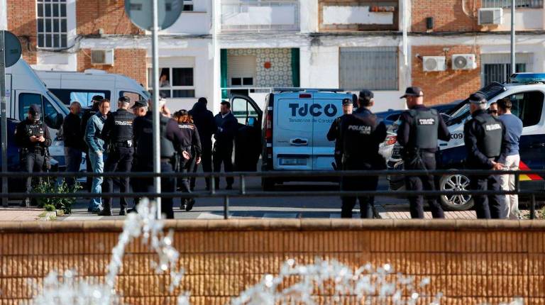 <i>Agentes de la Policía Nacional junto a la furgoneta del tanatorio dispuesta para el traslado del cadáver de la mujer asesinada en el barrio de la Fuensanta. / Madero Cubero / Europa Press.</i>