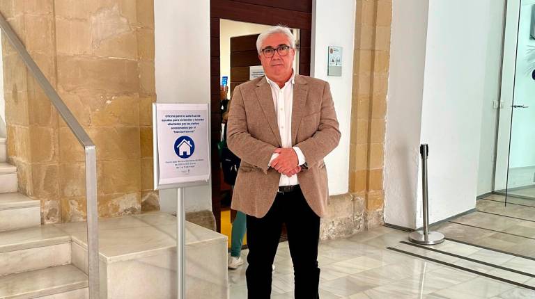 <i>Bartolomé Cruz junto al cartel que señaliza la sala en la que se gestionan las ayudas. / Ayuntamiento de Baeza.</i>